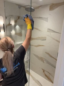 A cleaner wiping the shower glass
